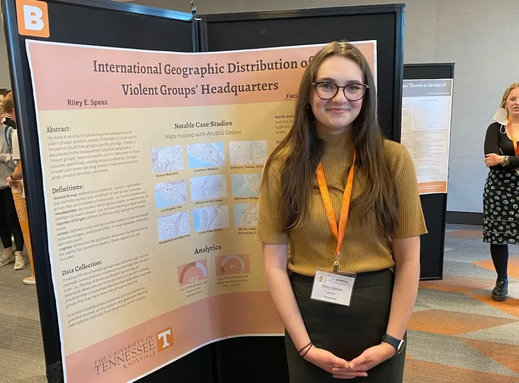 A female student stands in front of a research poster at a symposium